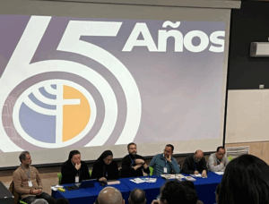 Religiosas y religiosos sentados como expositores en una mesa, con un cartel detrás